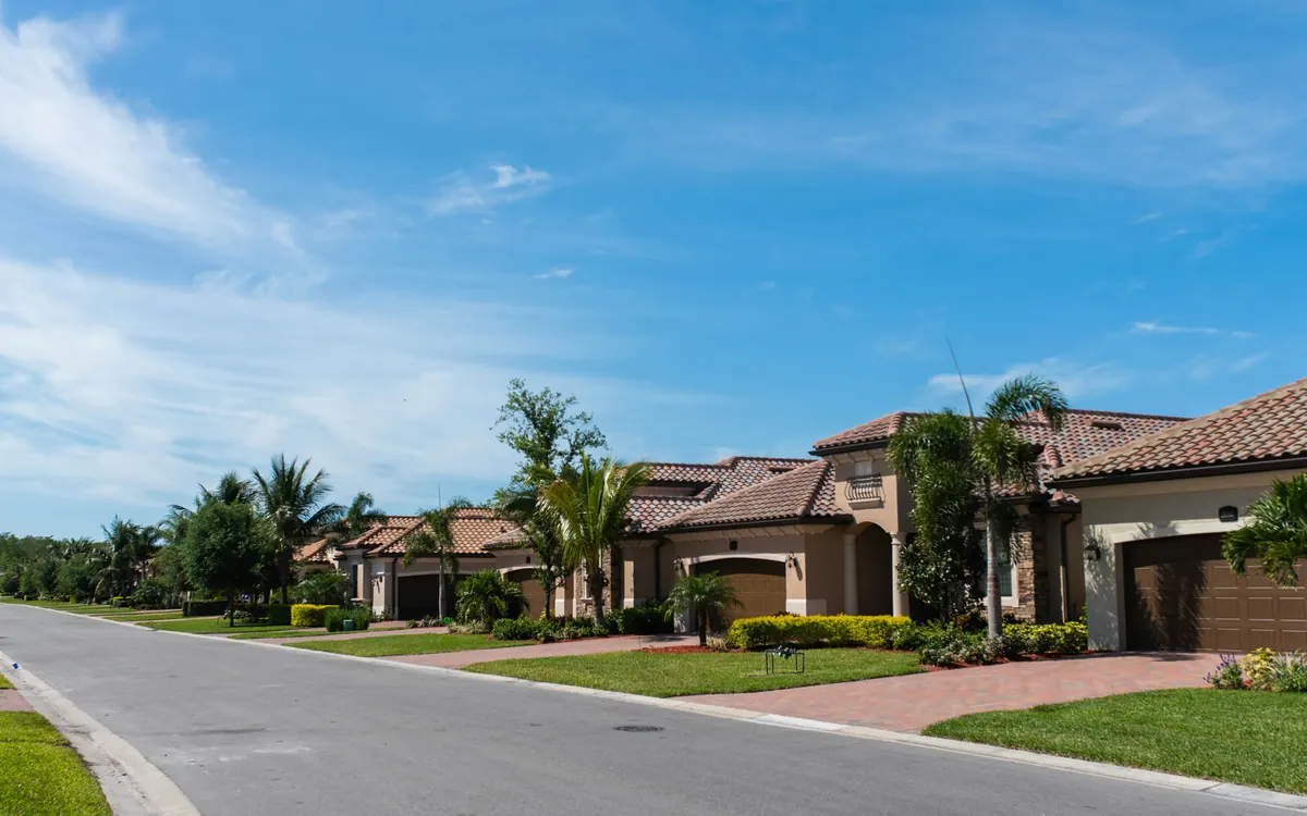 A quiet Florida residential street of tile-roof homes with palms and manicured lawns